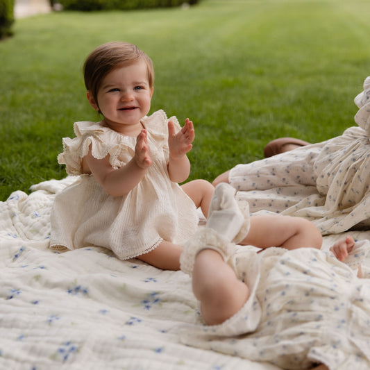 Two young children sitting on a blanket in a garden