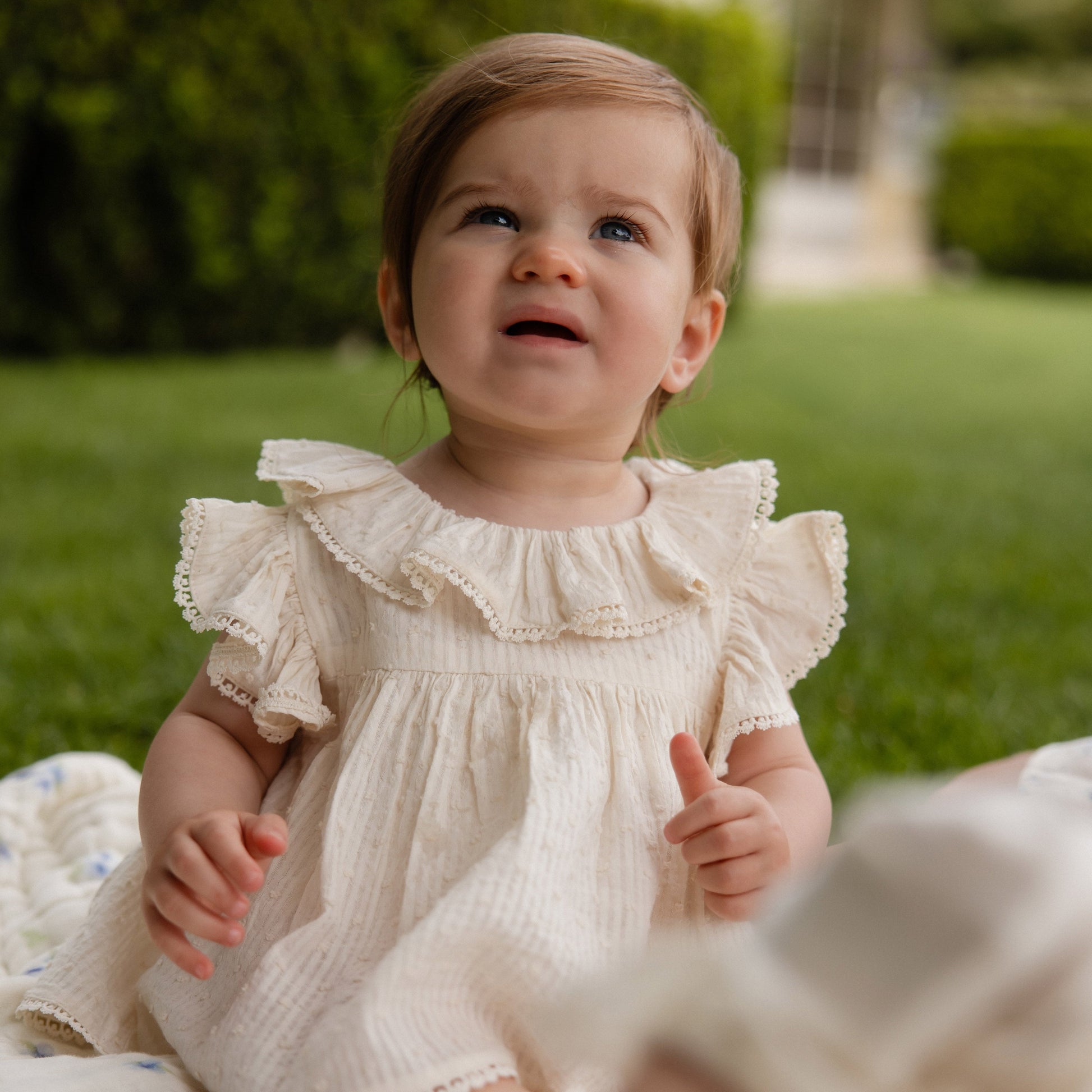 Baby in a white dress sitting on grass