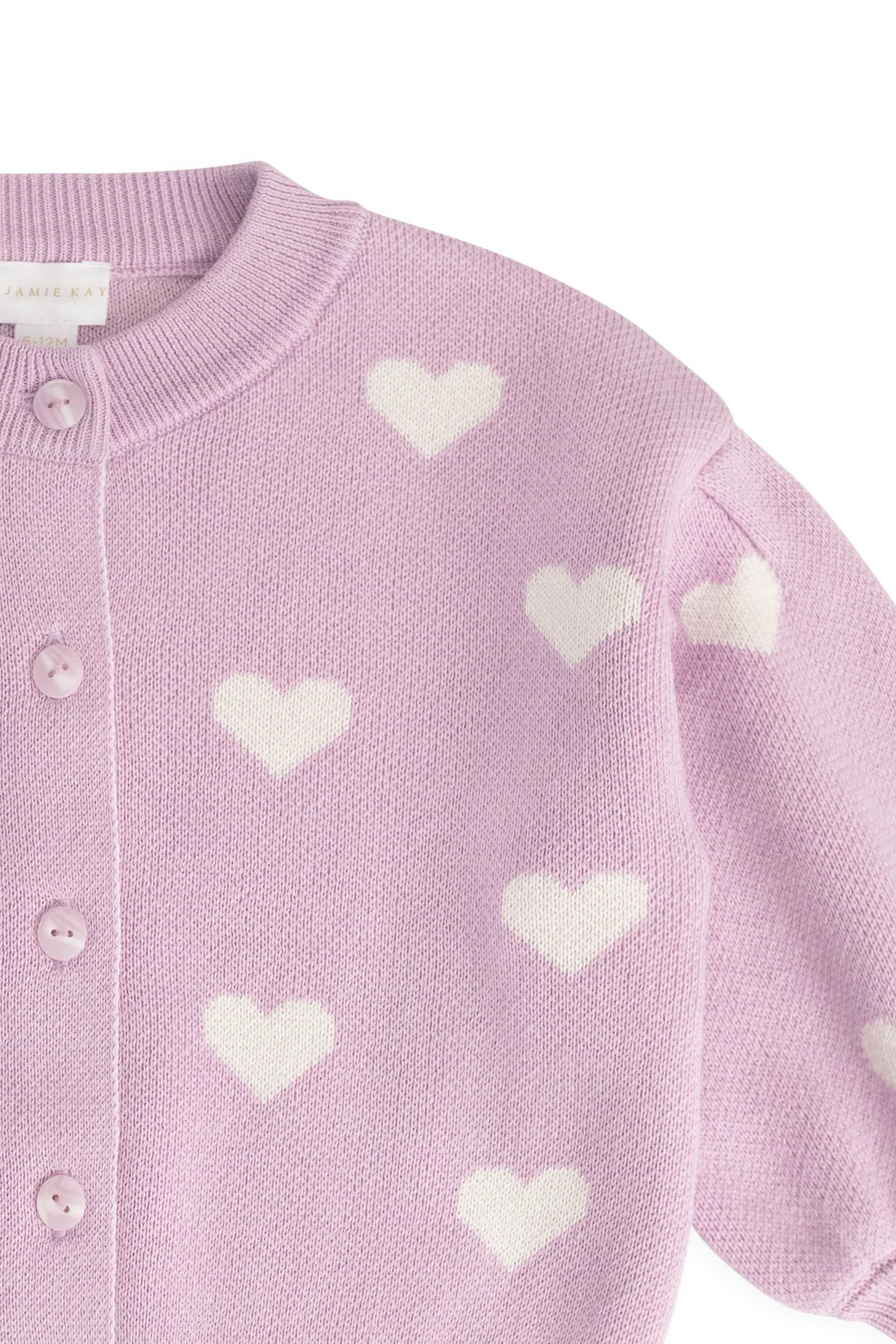 A close-up of a light pink knit cardigan with white heart motifs, featuring a ribbed collar and front button closure.