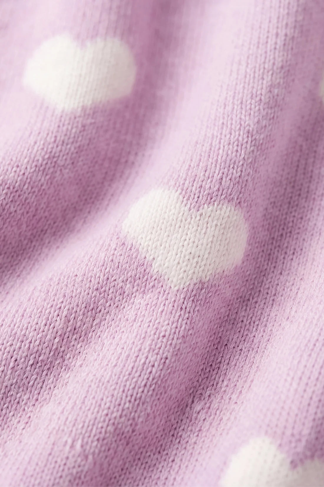 Close-up of a soft knit fabric in light pink with white heart motifs.