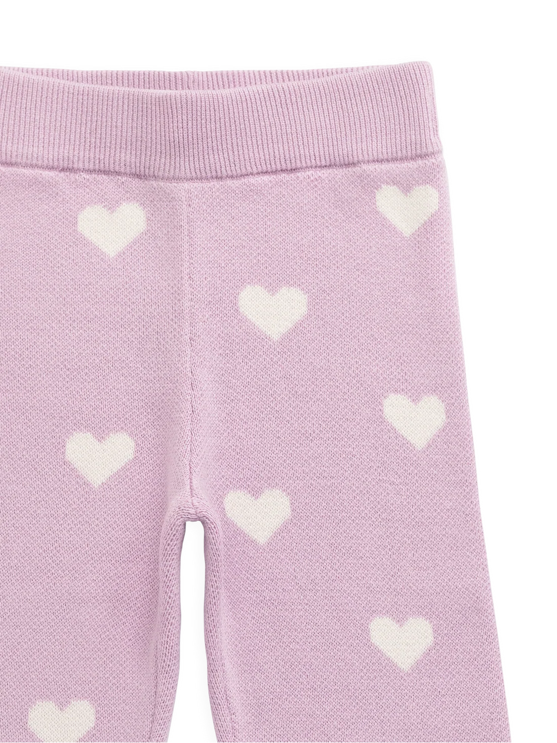 Close-up of a pair of light pink knit leggings with a white heart pattern, showing the ribbed waistband and leg texture.