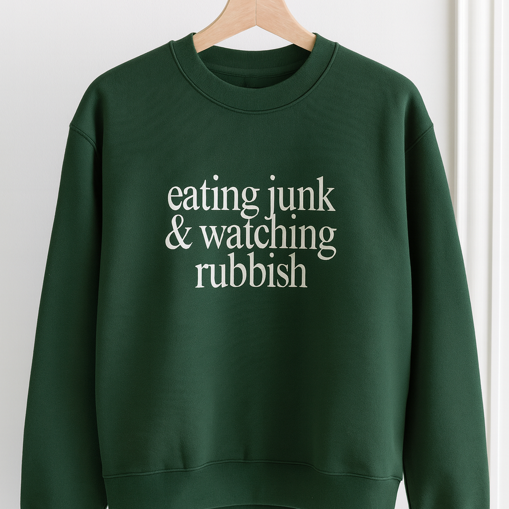 Green sweatshirt with text 'eating junk & watching rubbish' on a hanger against a white background