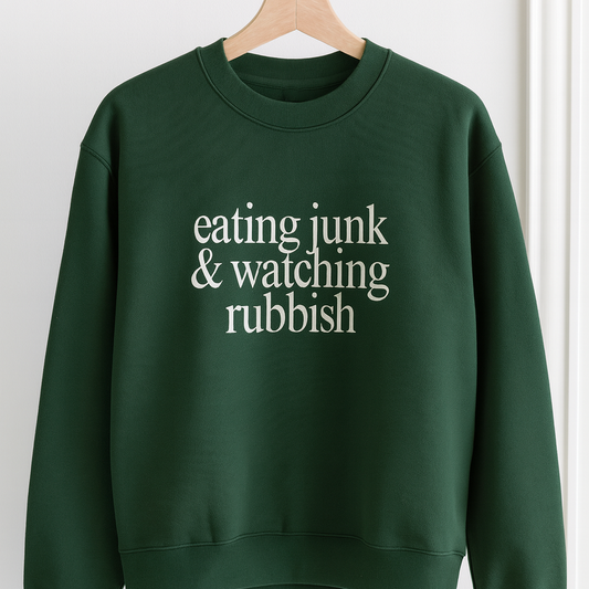 Green sweatshirt with text 'eating junk & watching rubbish' on a hanger against a white background