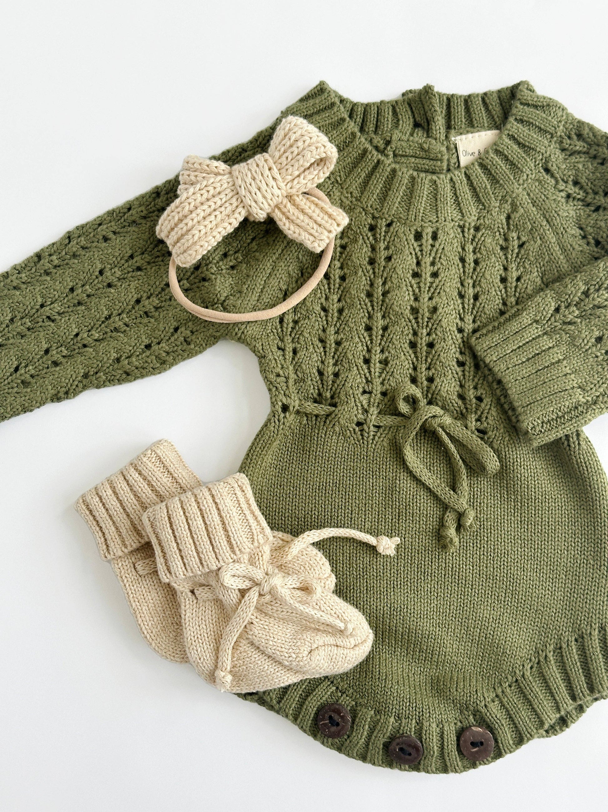 Green knitted baby outfit with beige headband and booties on a white background