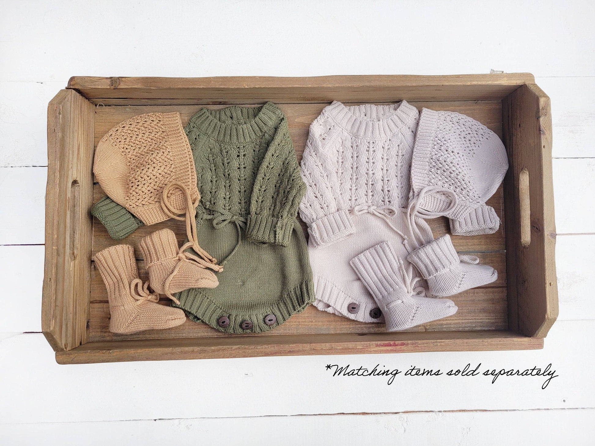 Set of baby knitted hats and booties in beige, green, and white on a wooden tray.