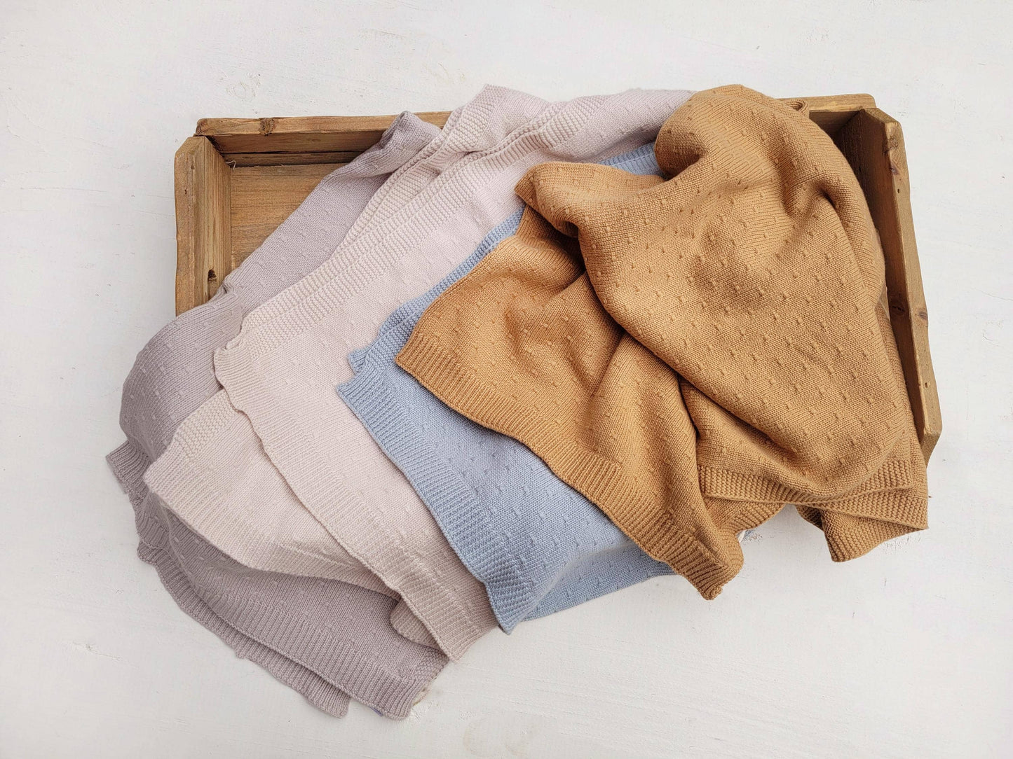 Stack of folded sweaters in various colors on a wooden tray.
