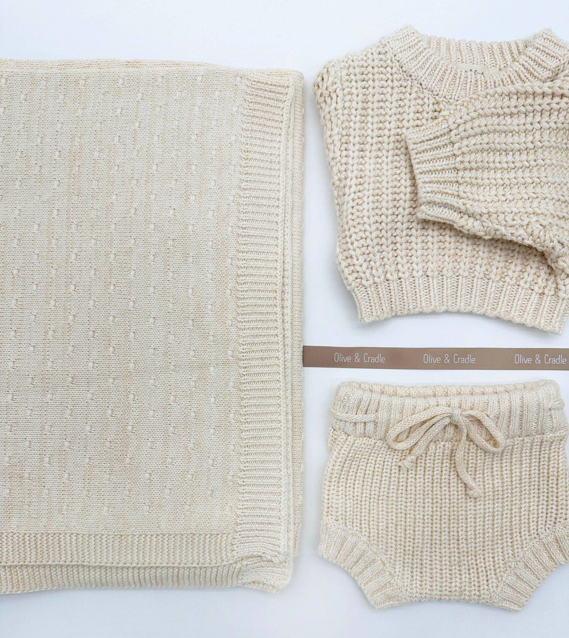 Beige knitted baby outfit with sweater, blanket, and shorts on a light background.