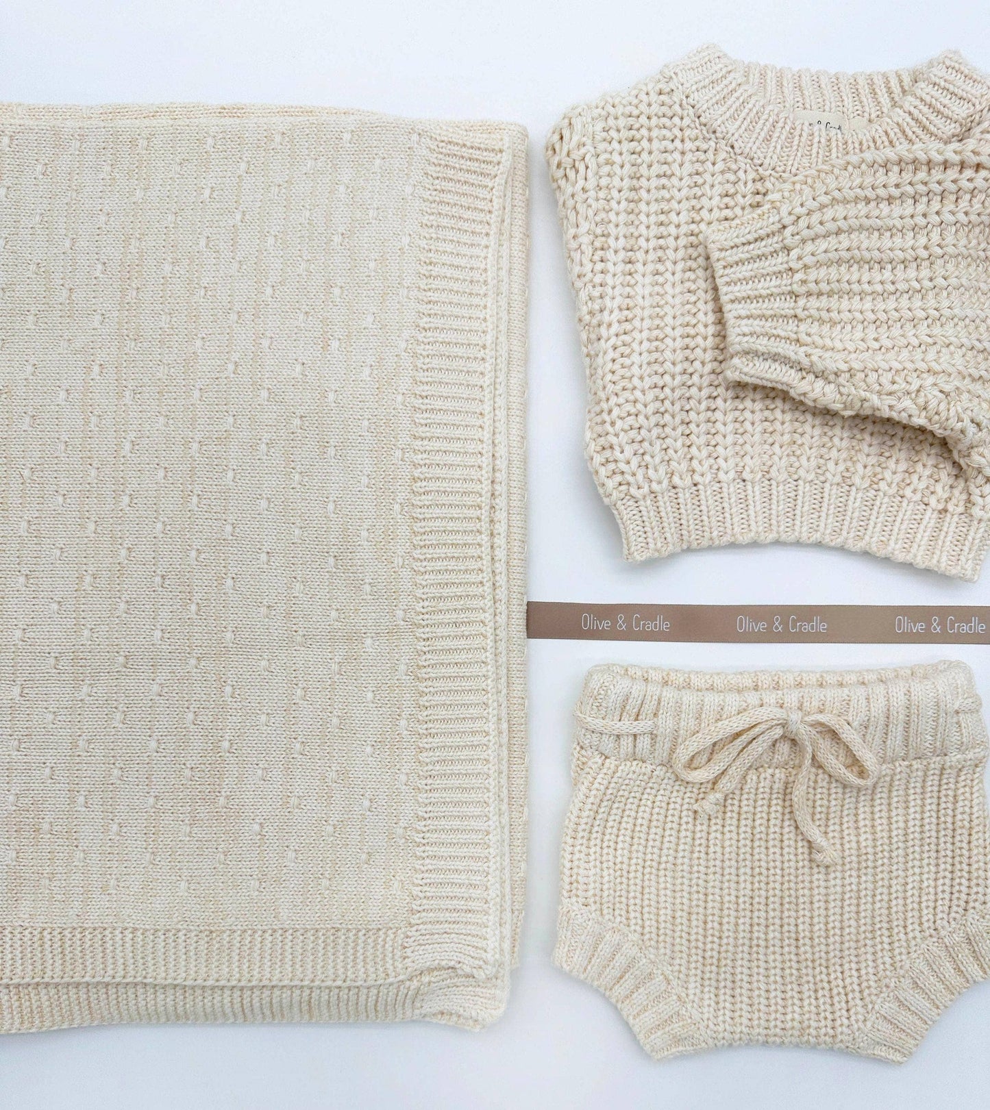 Beige knitted baby outfit with sweater, blanket, and shorts on a white background.