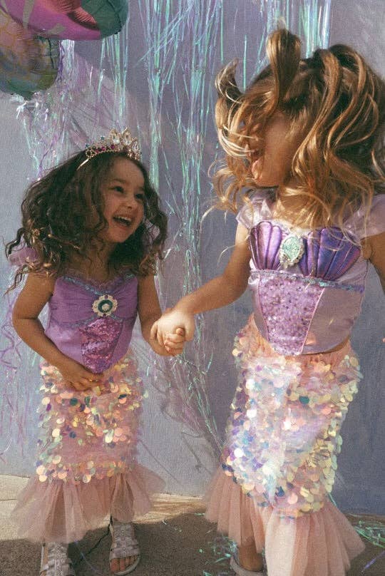 Two children in mermaid costumes playing together with a sparkly background.