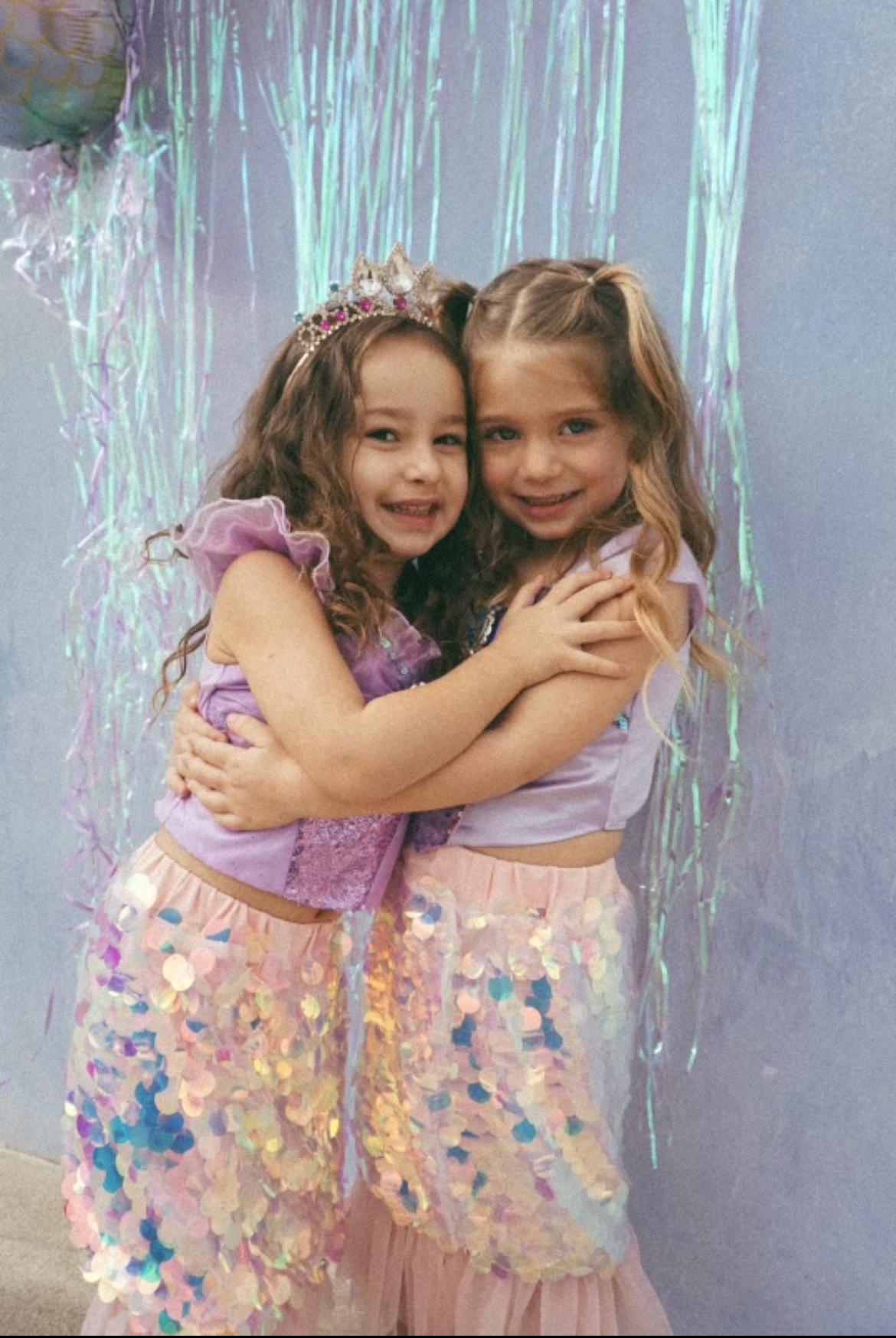 Two young girls hugging in front of a colorful curtain