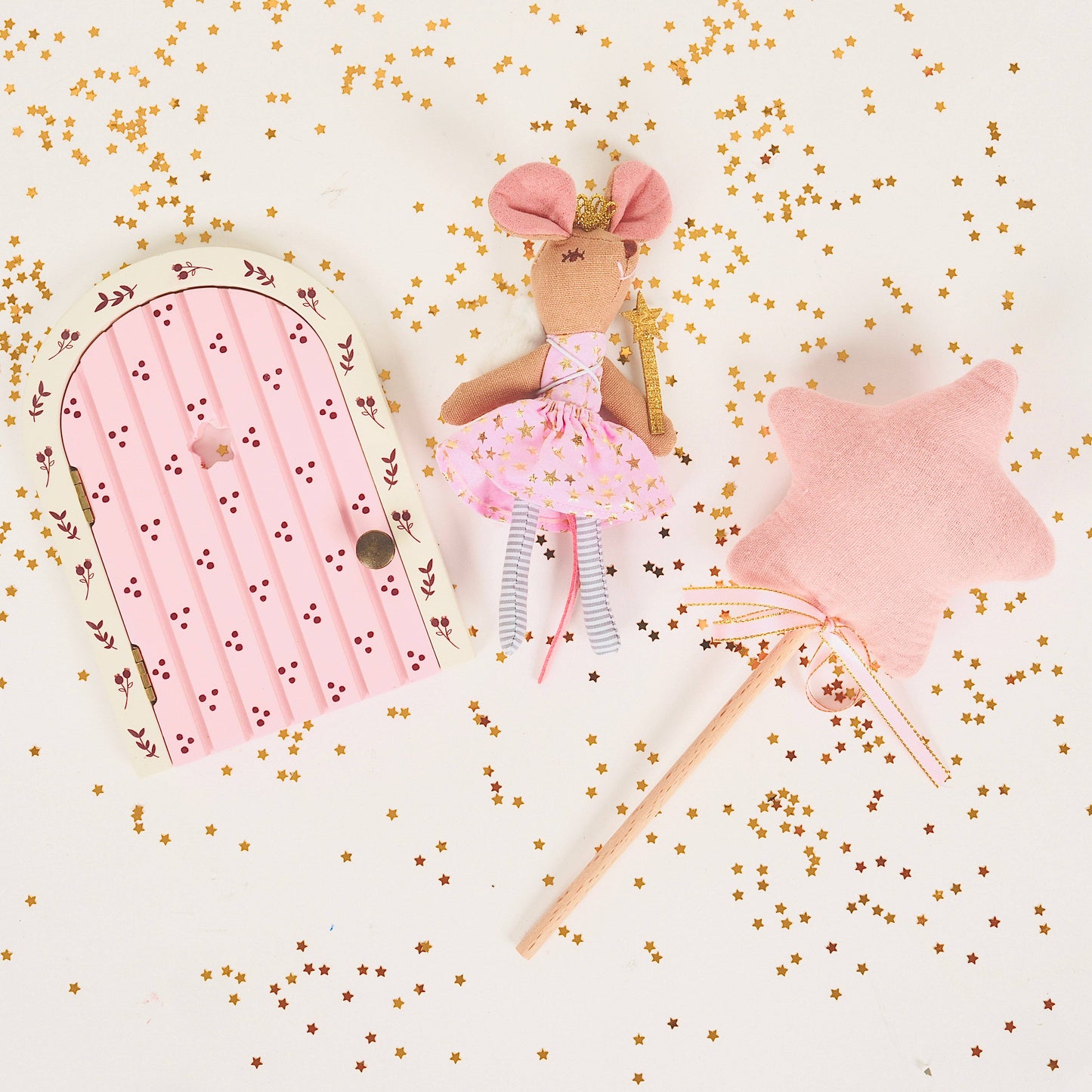 Fairy doll with pink dress and wand, pink fairy door, and pink star pillow on a white background with gold confetti.