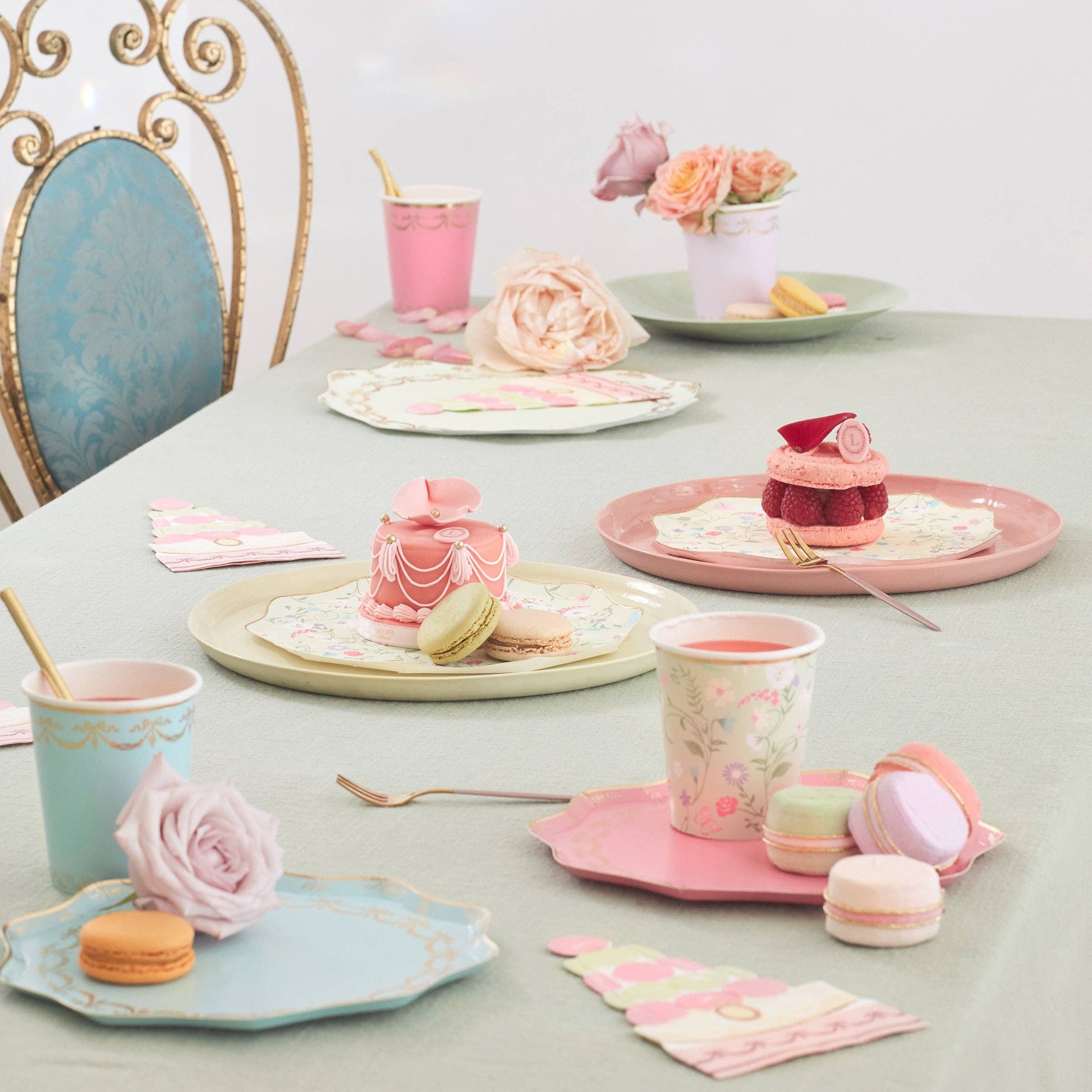 Pastel-themed tea party setup with cups, cookies, and flowers on a table.