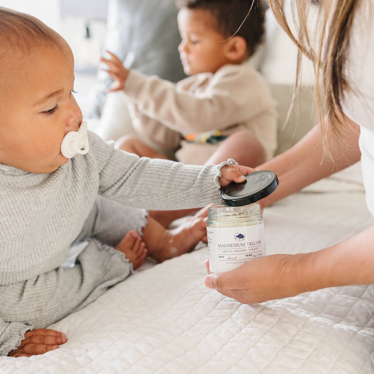 Baby holding a jar of baby food with another baby in the background