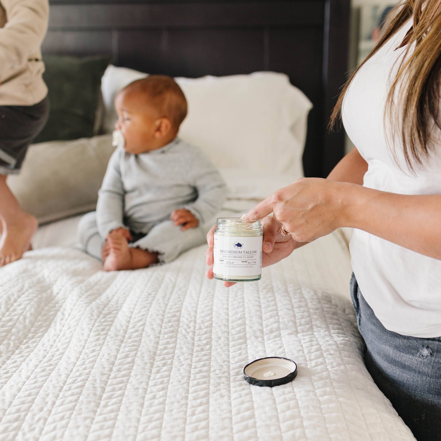 Person holding a candle on a bed with a baby sitting nearby
