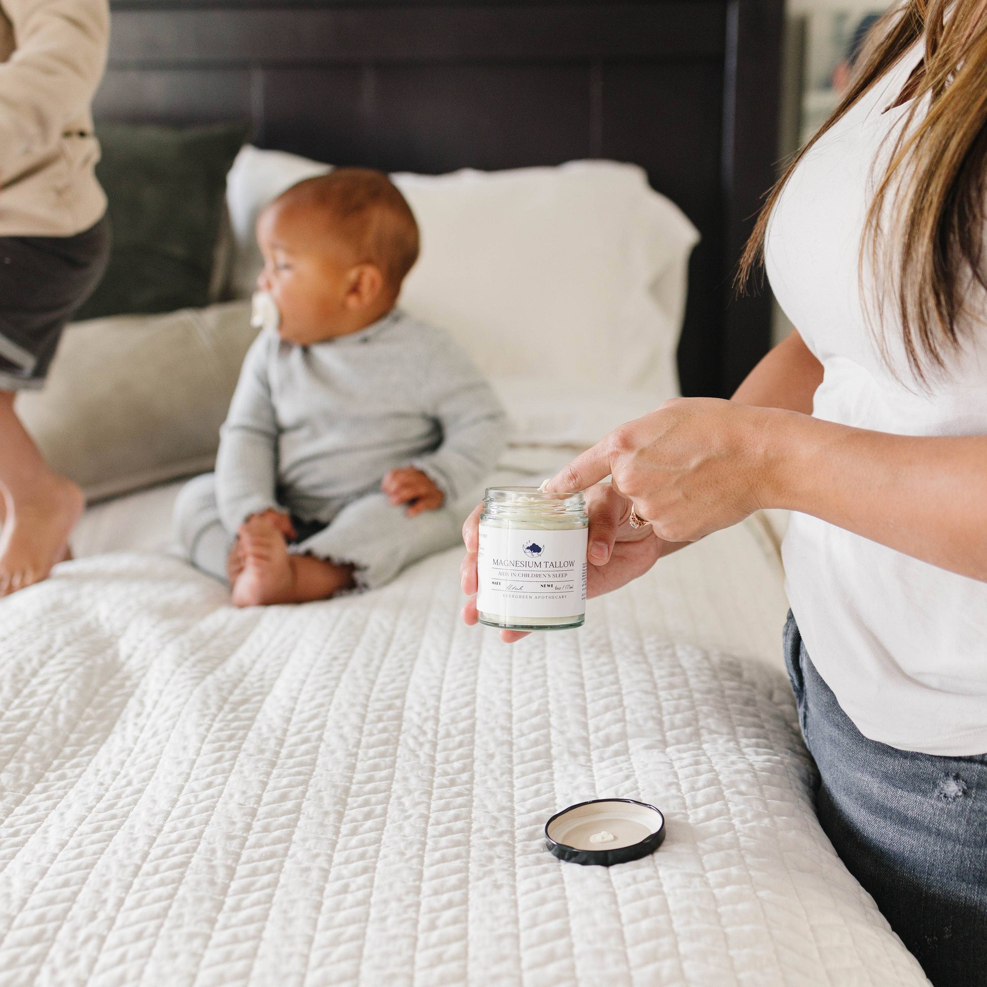 Person holding a candle on a bed with a baby sitting nearby