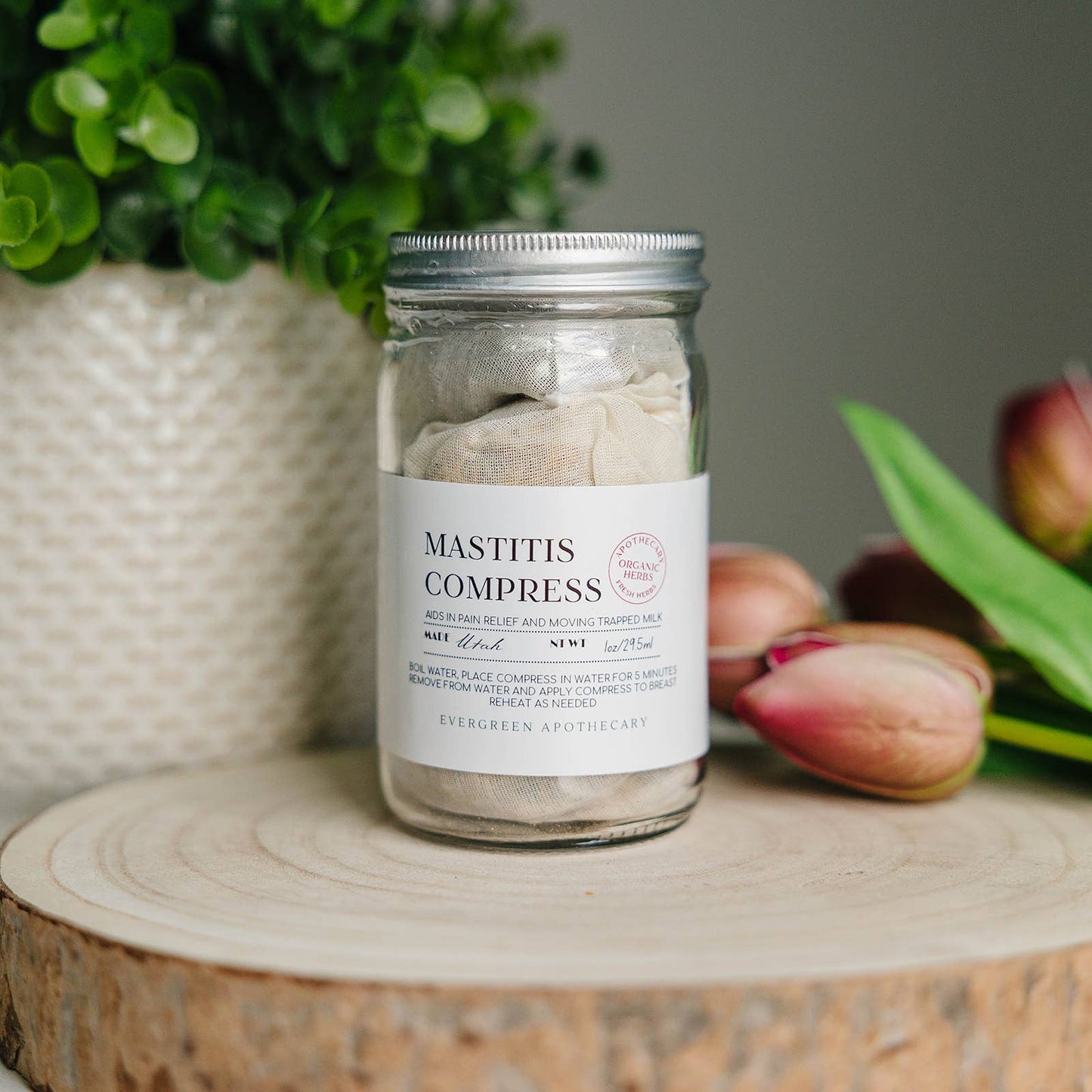 Jar of Mastitis Compress on a wooden surface with a plant and flowers in the background