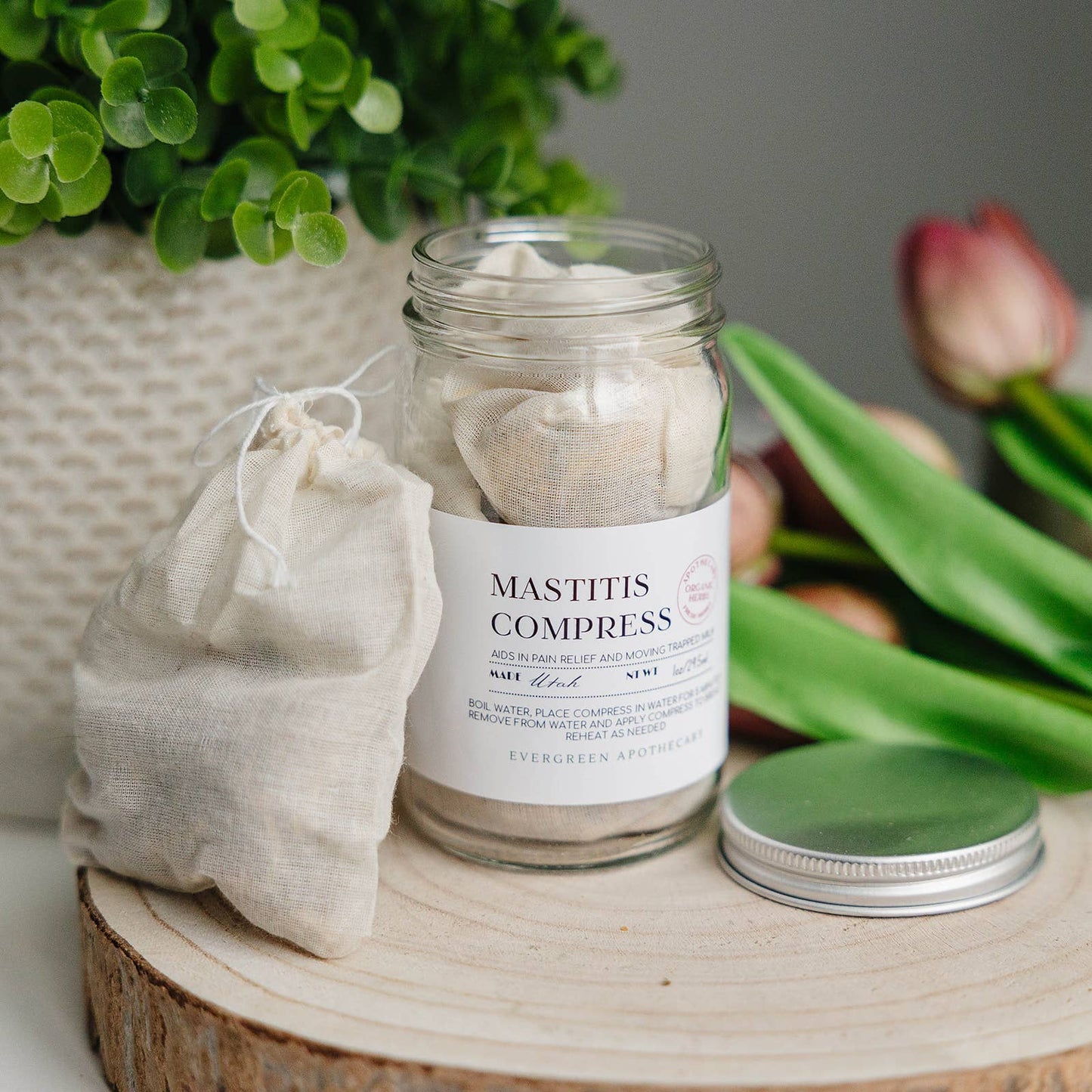 Jar of Mastitis Compresses with a label on a wooden surface, surrounded by greenery.