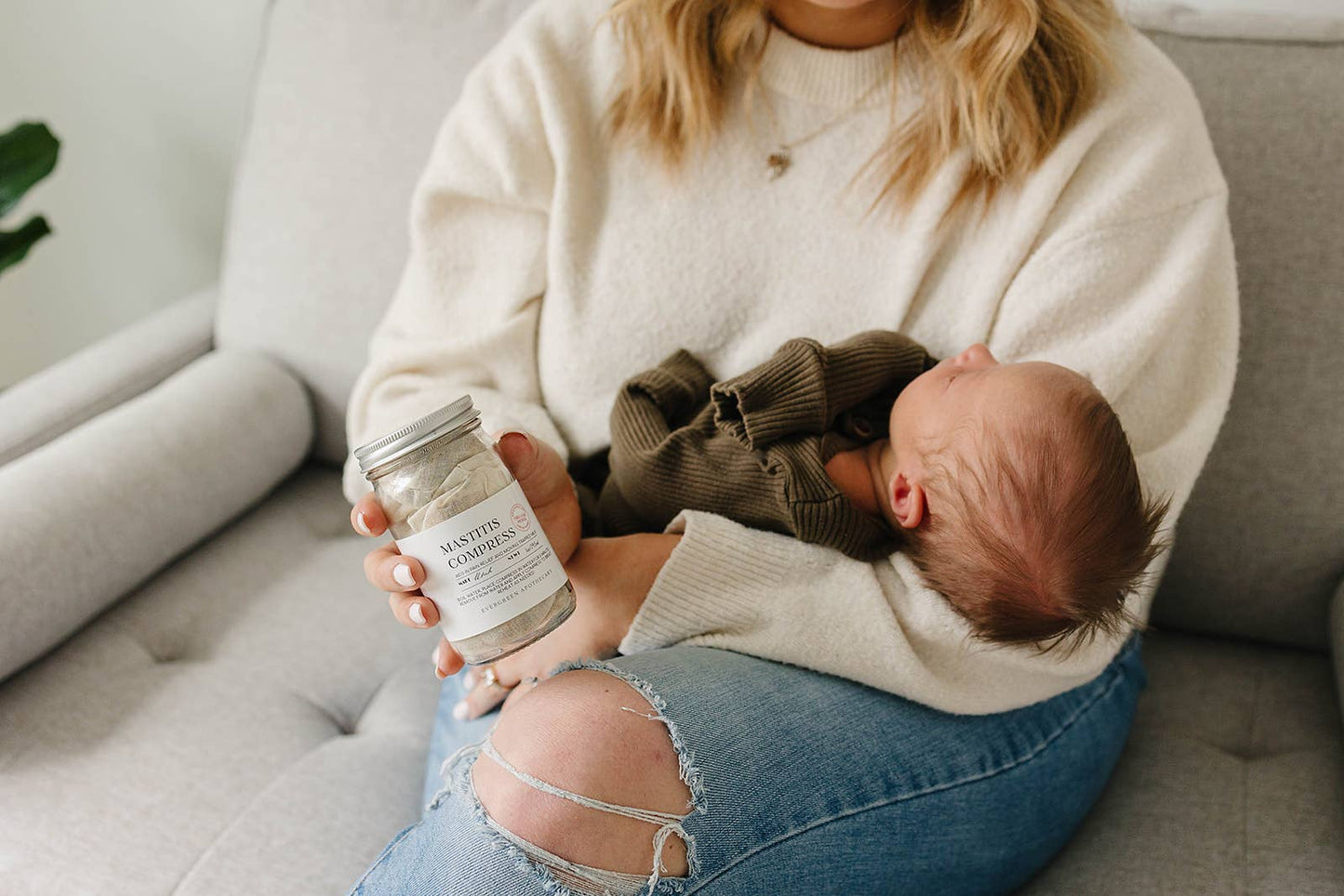 Woman holding a baby and a jar of baby food on a couch