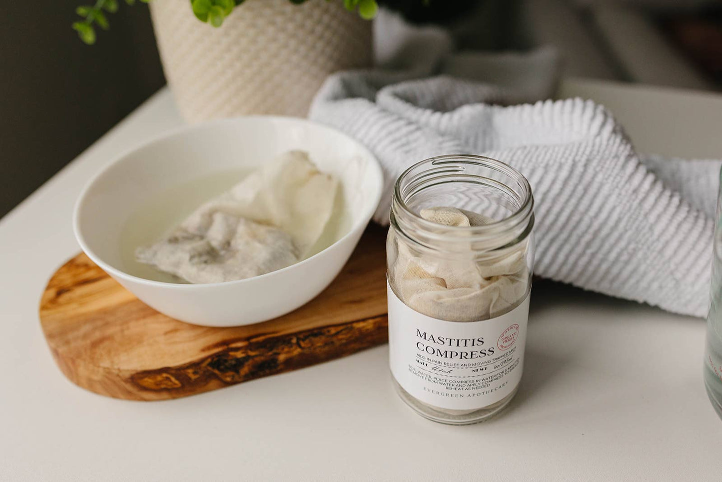 Manthia compresses in a jar and bowl on a table with a towel and plant in the background