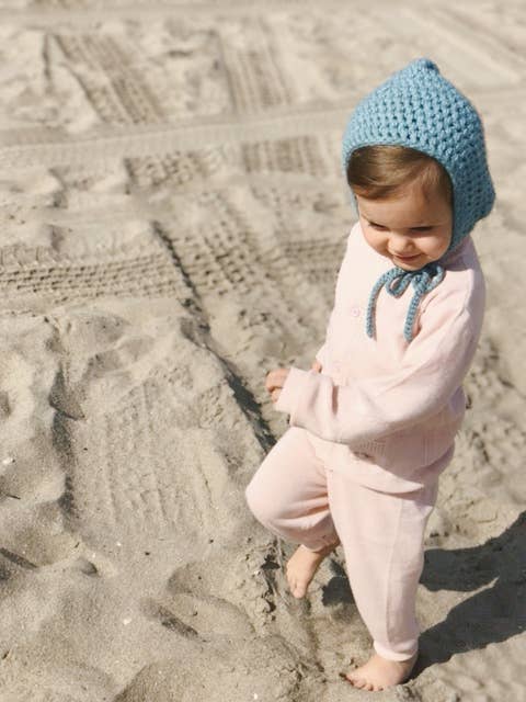 Child wearing a pink outfit and blue knitted hat on a sandy beach
