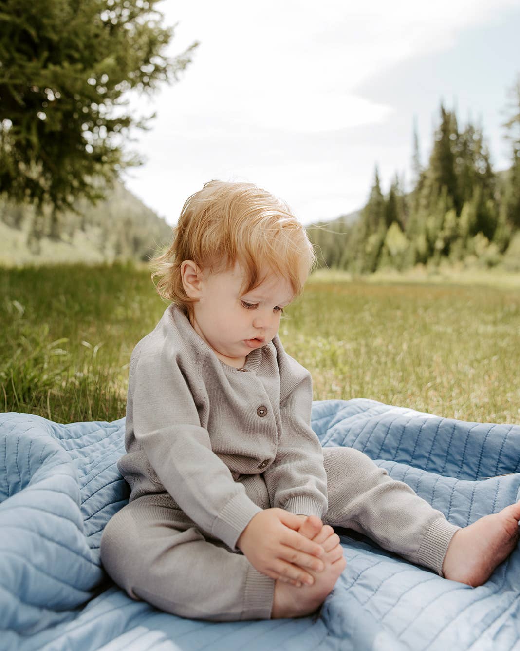 Child sitting on a blue blanket in a natural setting with trees and grass.