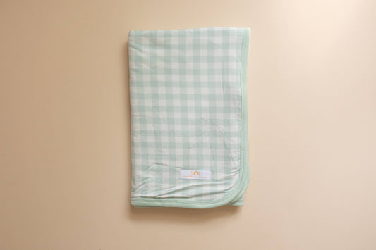 Green checkered blanket with a brand logo on a beige background