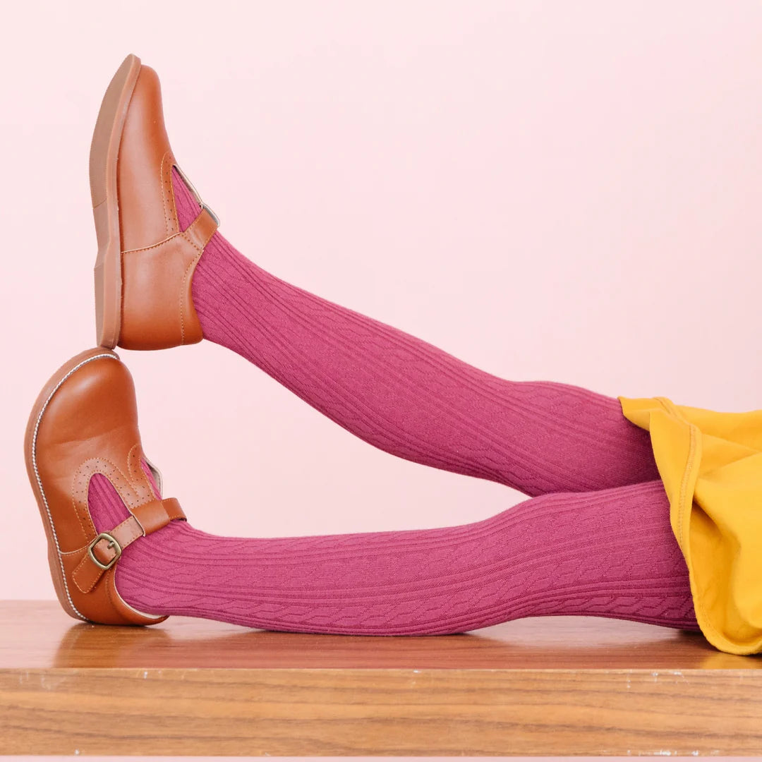 Person wearing pink knee-high socks and brown shoes on a pink background