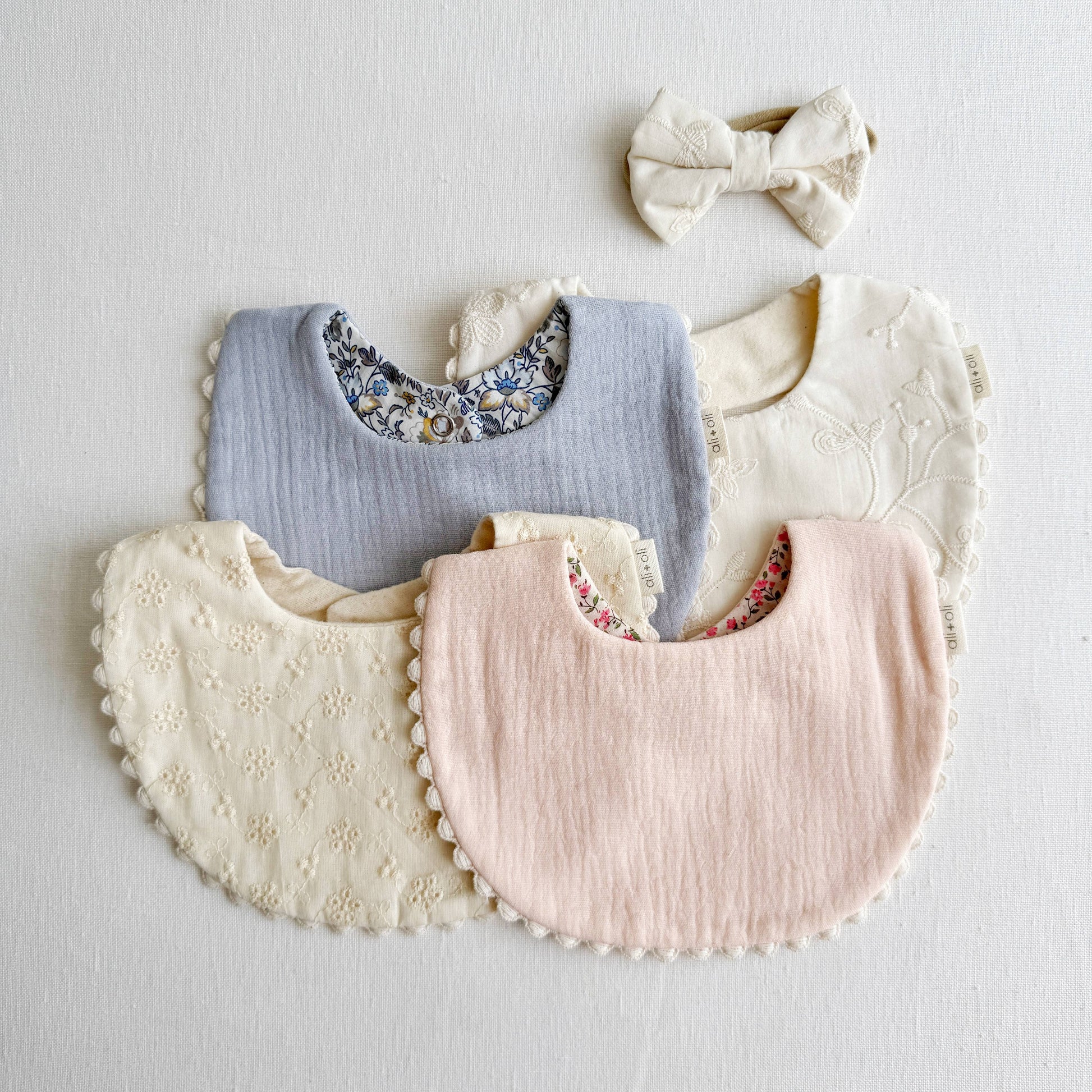 Set of baby bibs and a headband on a light gray background