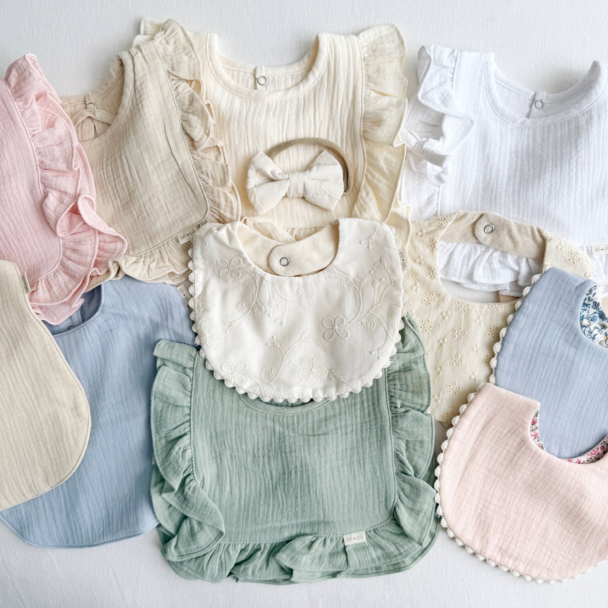 Collection of baby bibs and rompers in various colors on a light background
