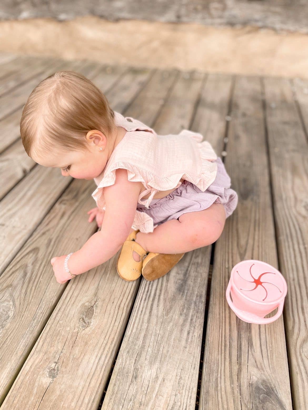 Baby sitting on a wooden floor with a pink cupcake-shaped object nearby