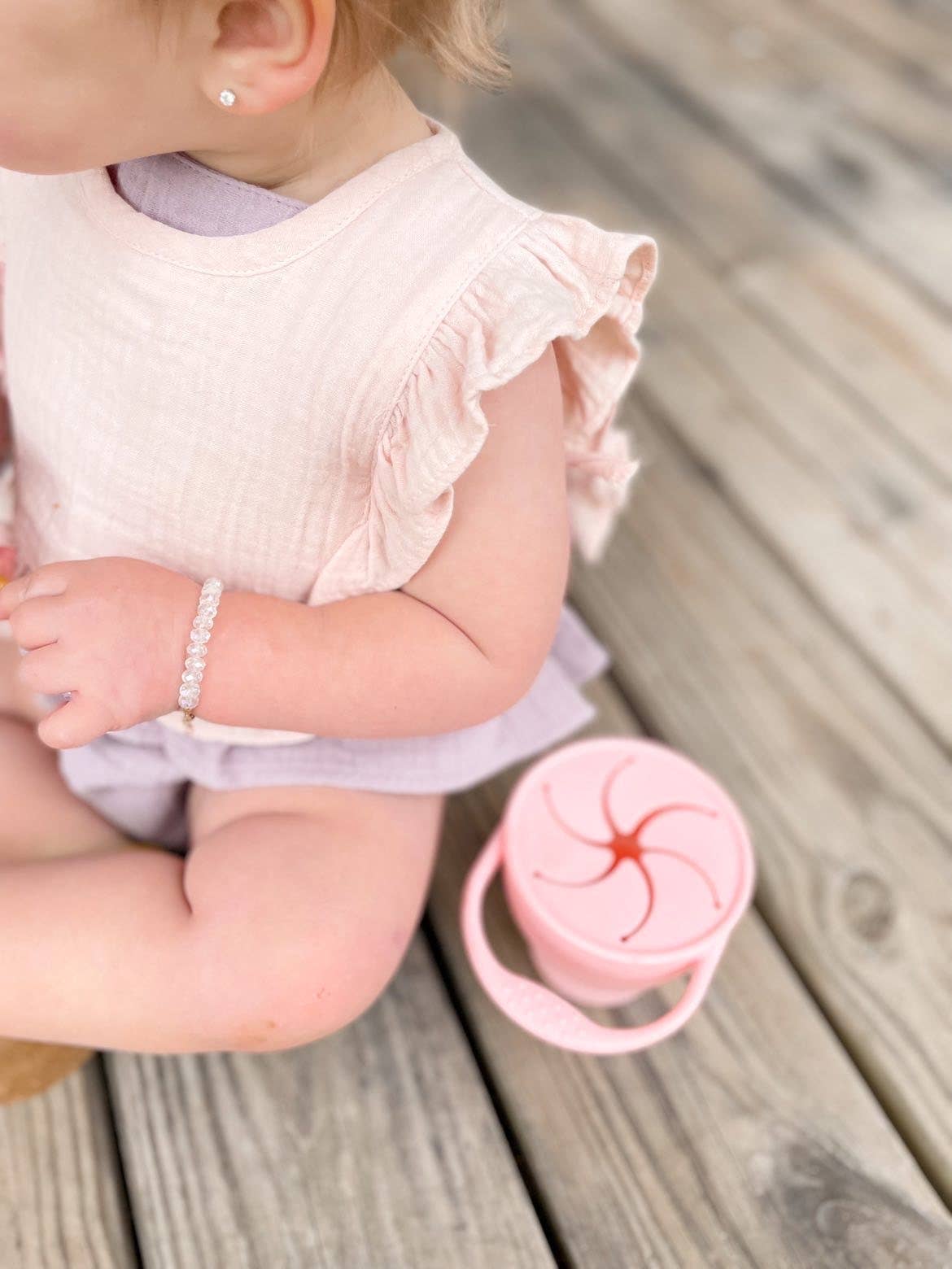 Child sitting on a wooden floor with a pink sippy cup nearby