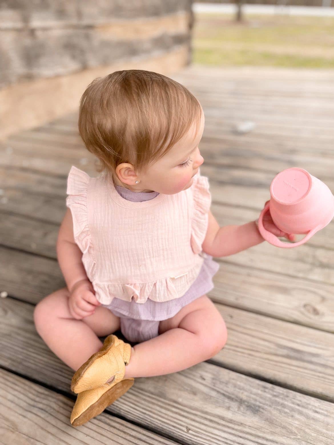 Child sitting on a wooden deck holding a pink cup