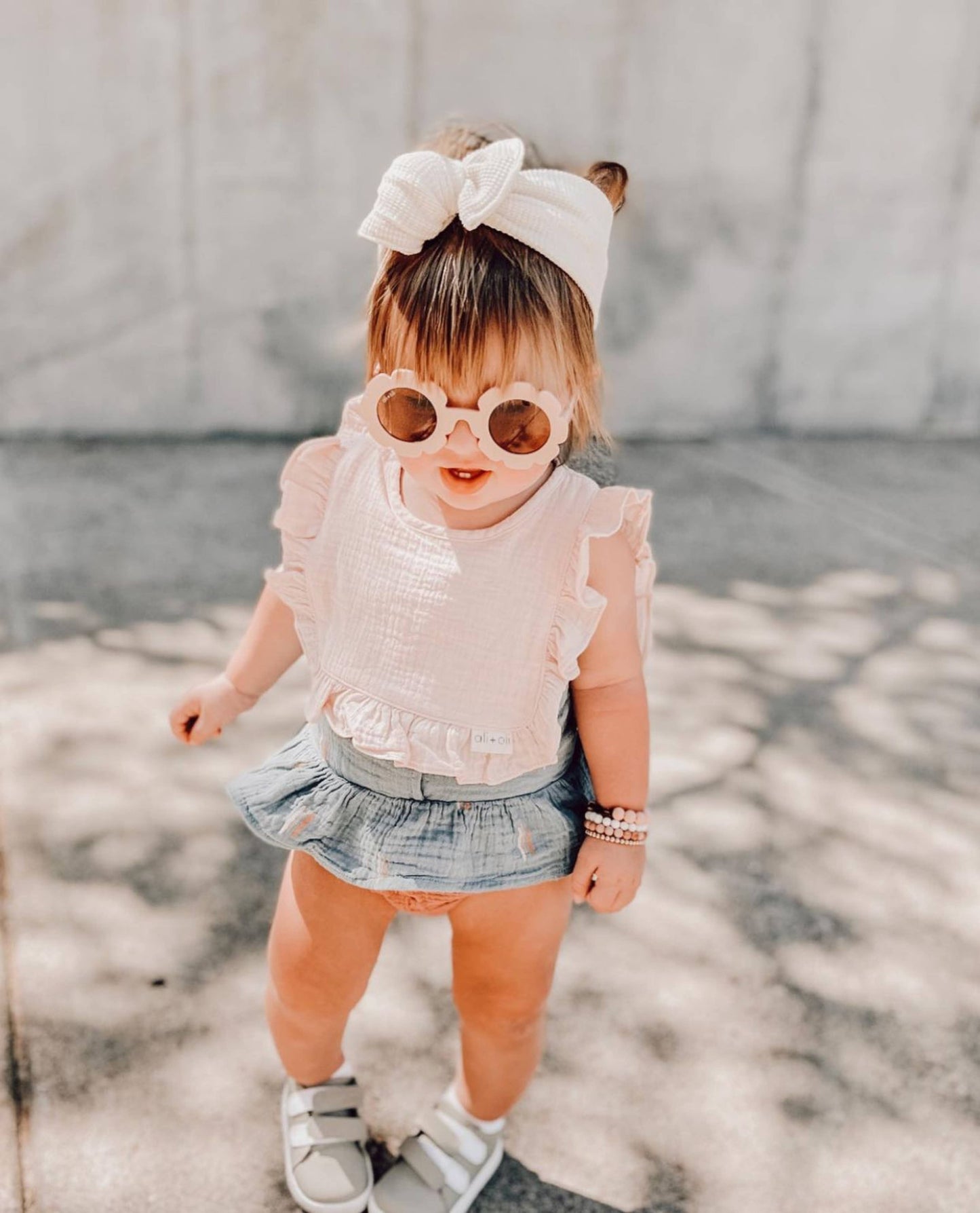 Child wearing a white top, denim skirt, and sunglasses with a white bow headband.