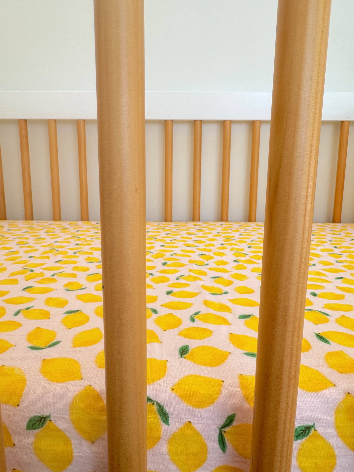 Crib with yellow lemon patterned sheet and wooden sides