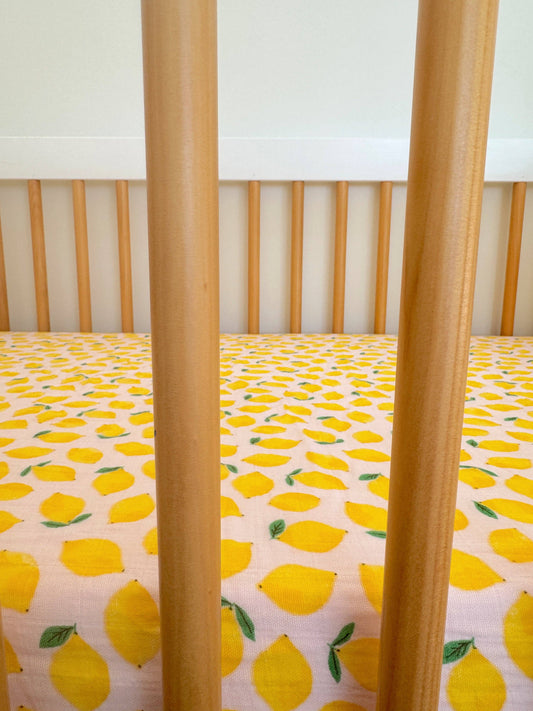 Crib with yellow lemon patterned sheet and wooden sides