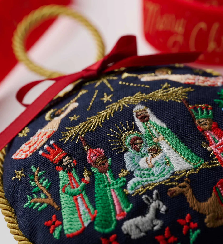 Embroidered nativity scene Christmas ornament with red ribbon on a red background