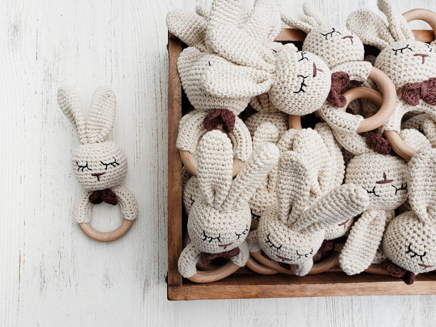 Wooden box filled with crocheted rabbit toys with wooden rings on a light wooden surface.