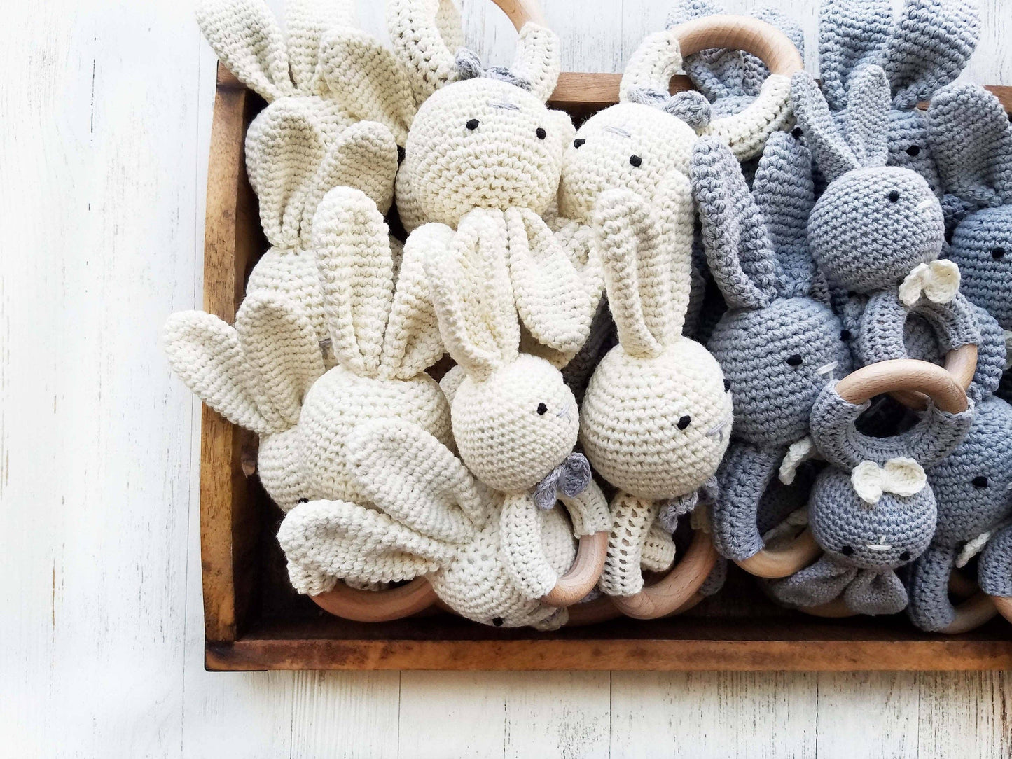 Wooden tray with crocheted bunny toys in white and gray on a light wooden surface.