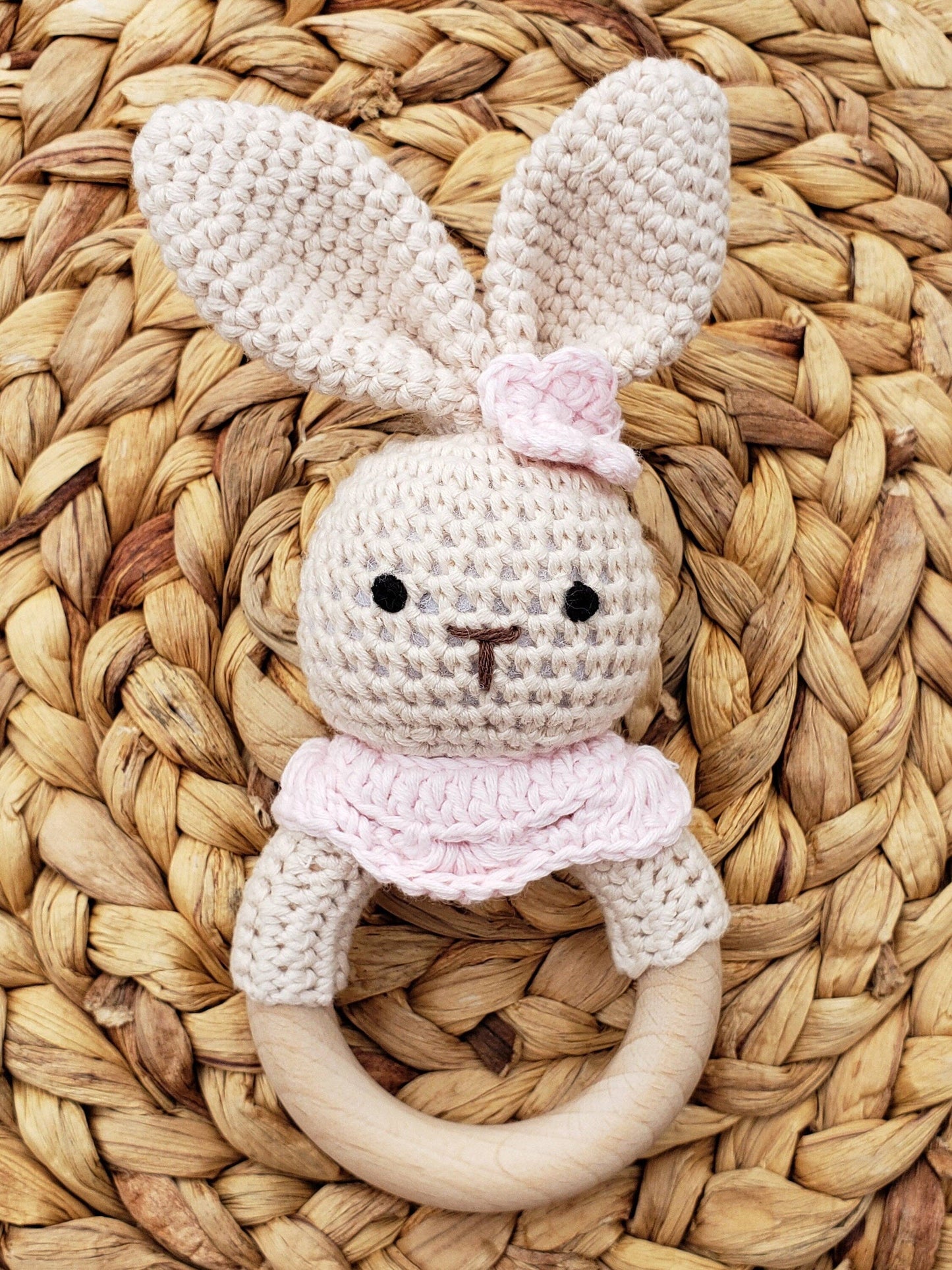 Crocheted bunny toy with a wooden ring on a woven mat