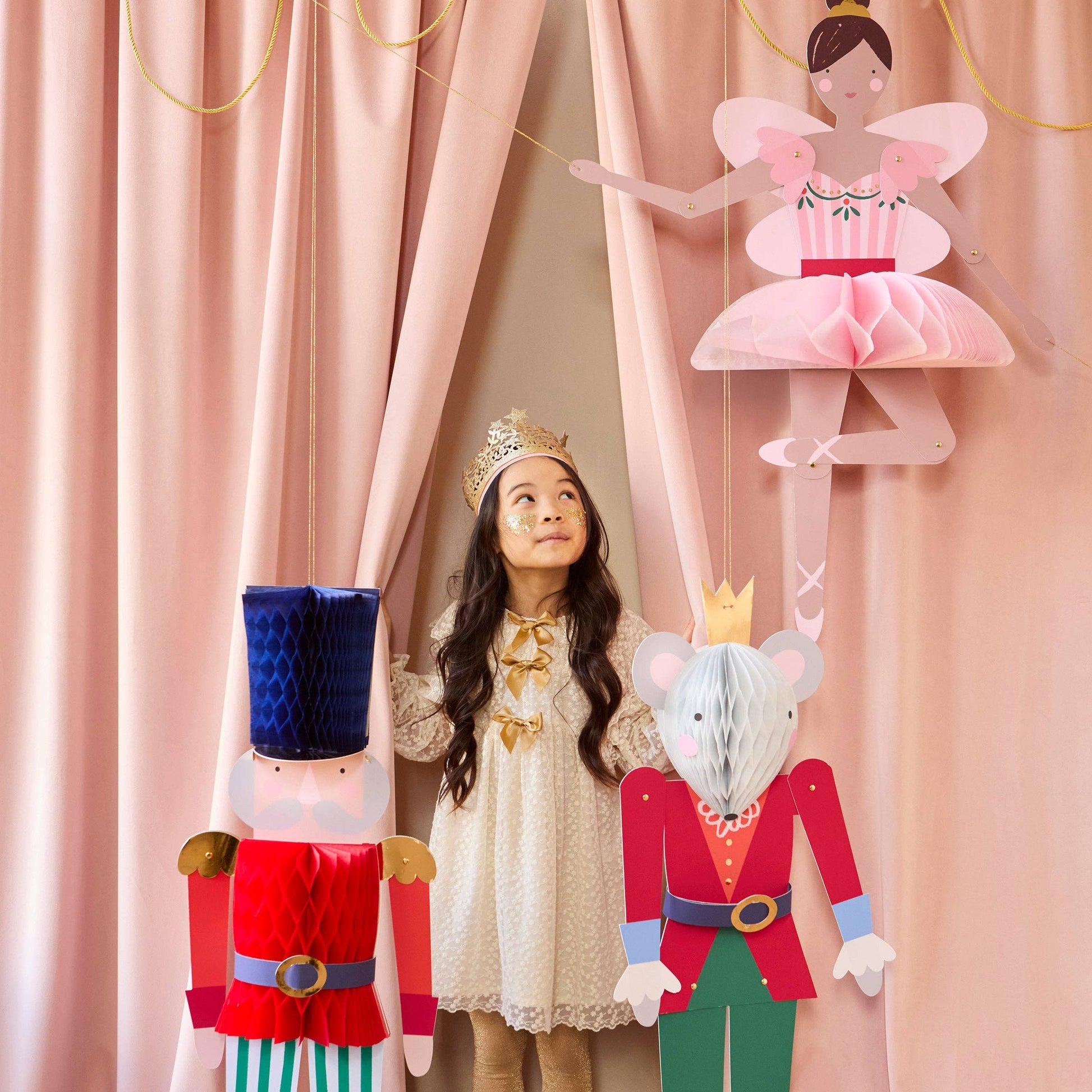 Child in a princess costume standing behind pink curtains with fairy and mouse king cutouts.