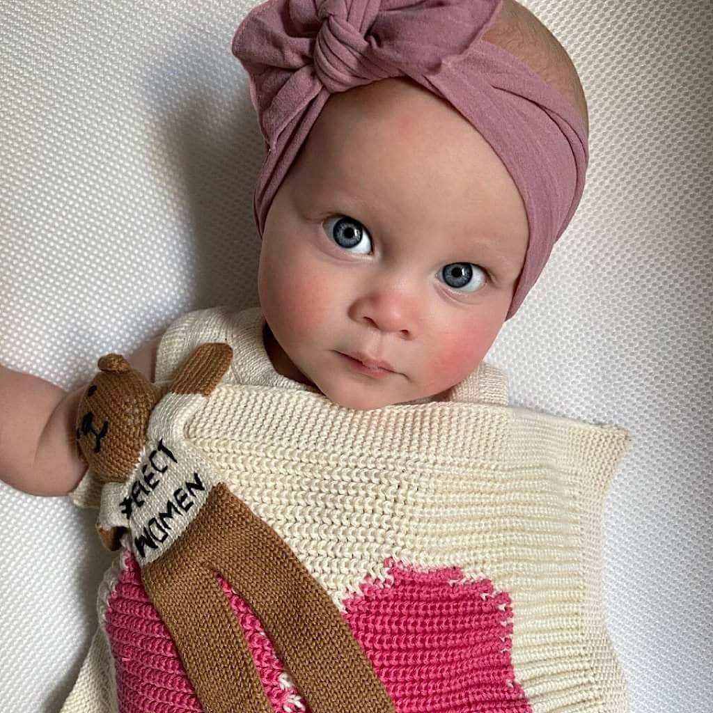 Baby wrapped in a knitted blanket with a pink heart design, wearing a pink headband.