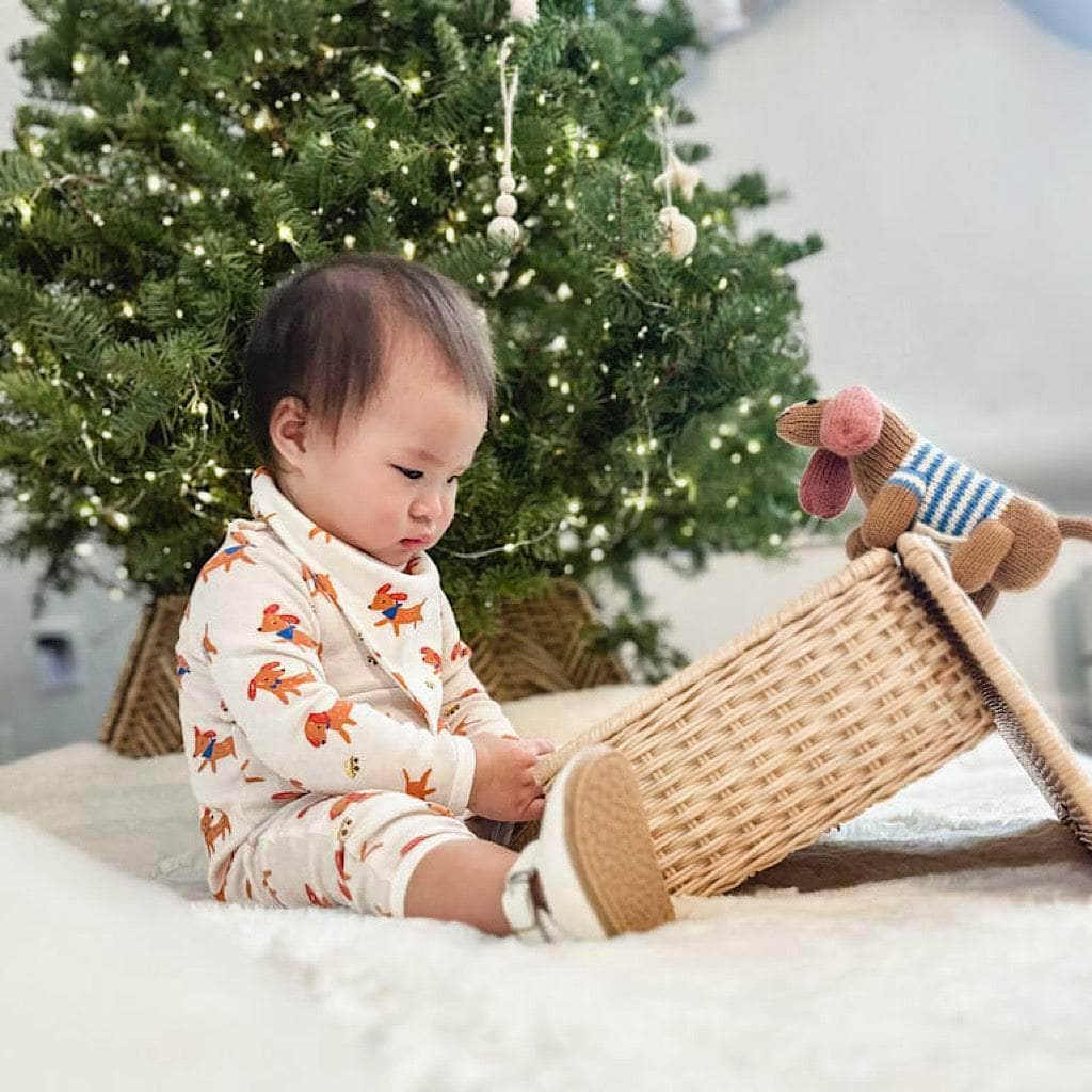 Baby playing with a woven toy in front of a decorated Christmas tree.