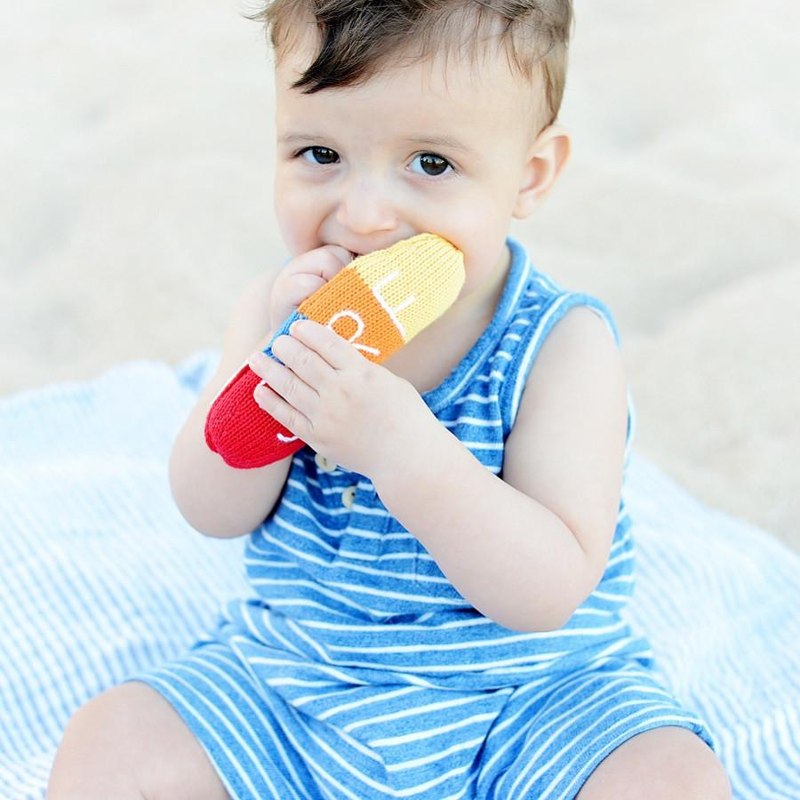 Baby holding a colorful teething toy with a plain background