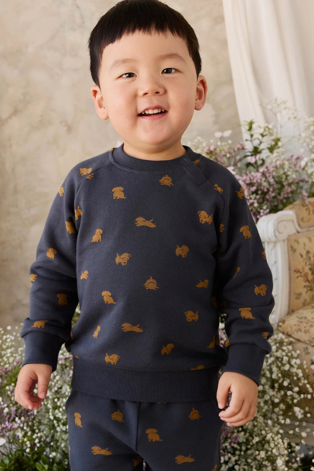 Child wearing a navy blue sweater with small yellow patterns, standing in a garden setting.
