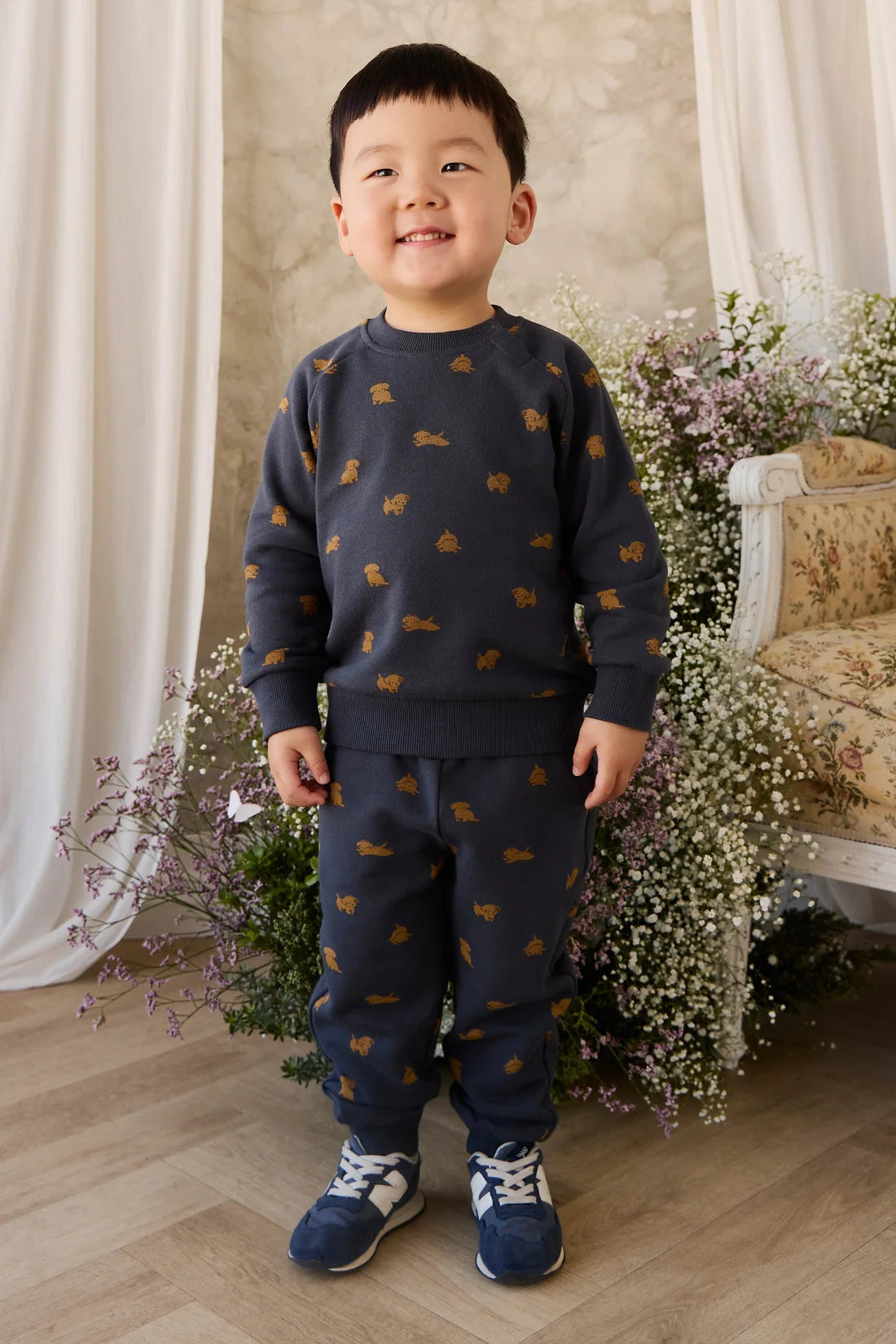 Child wearing a navy sweater and pants with small patterns, standing in a decorated room with flowers and a chair.