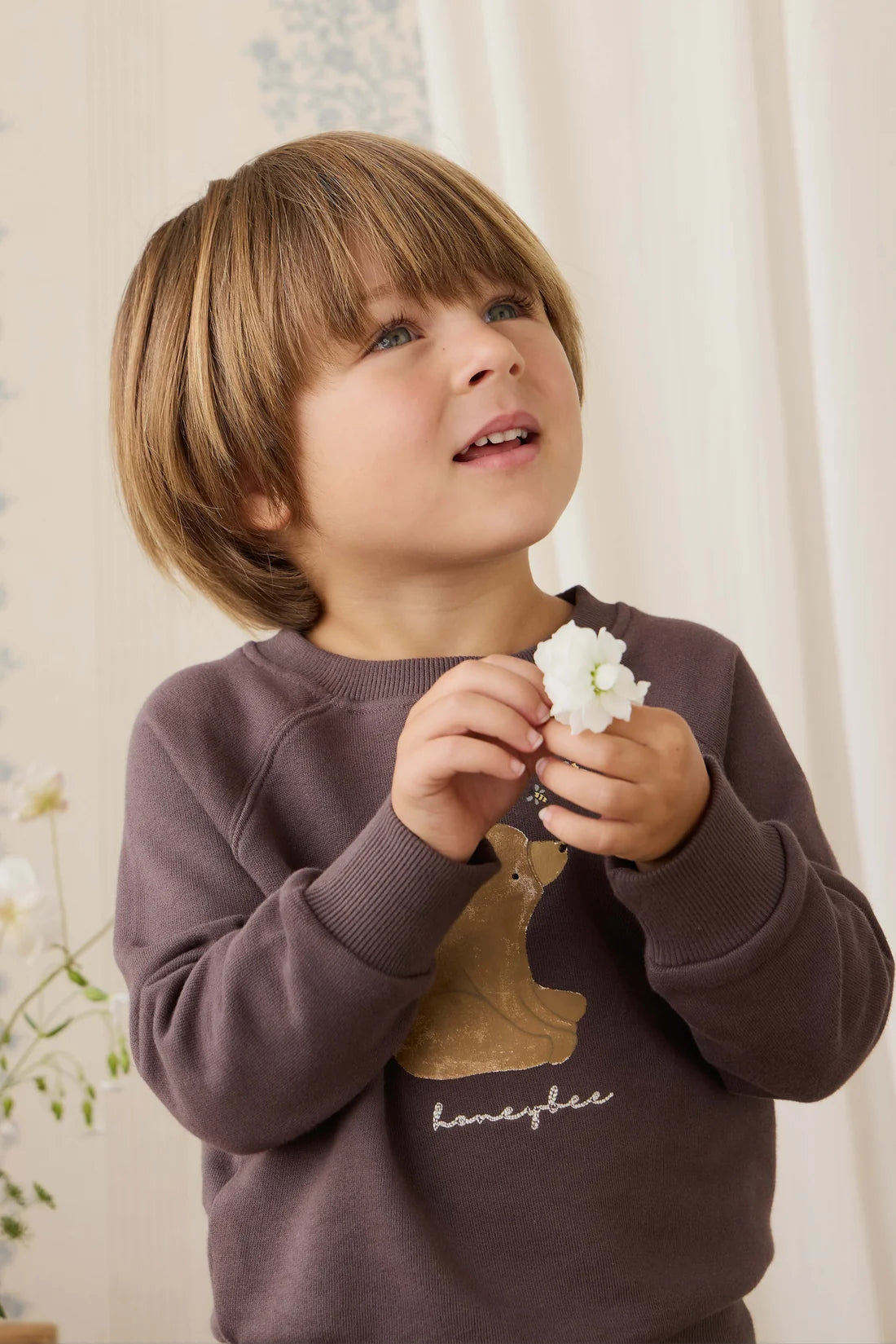 Child wearing a purple sweatshirt with a bear design, holding a white flower.