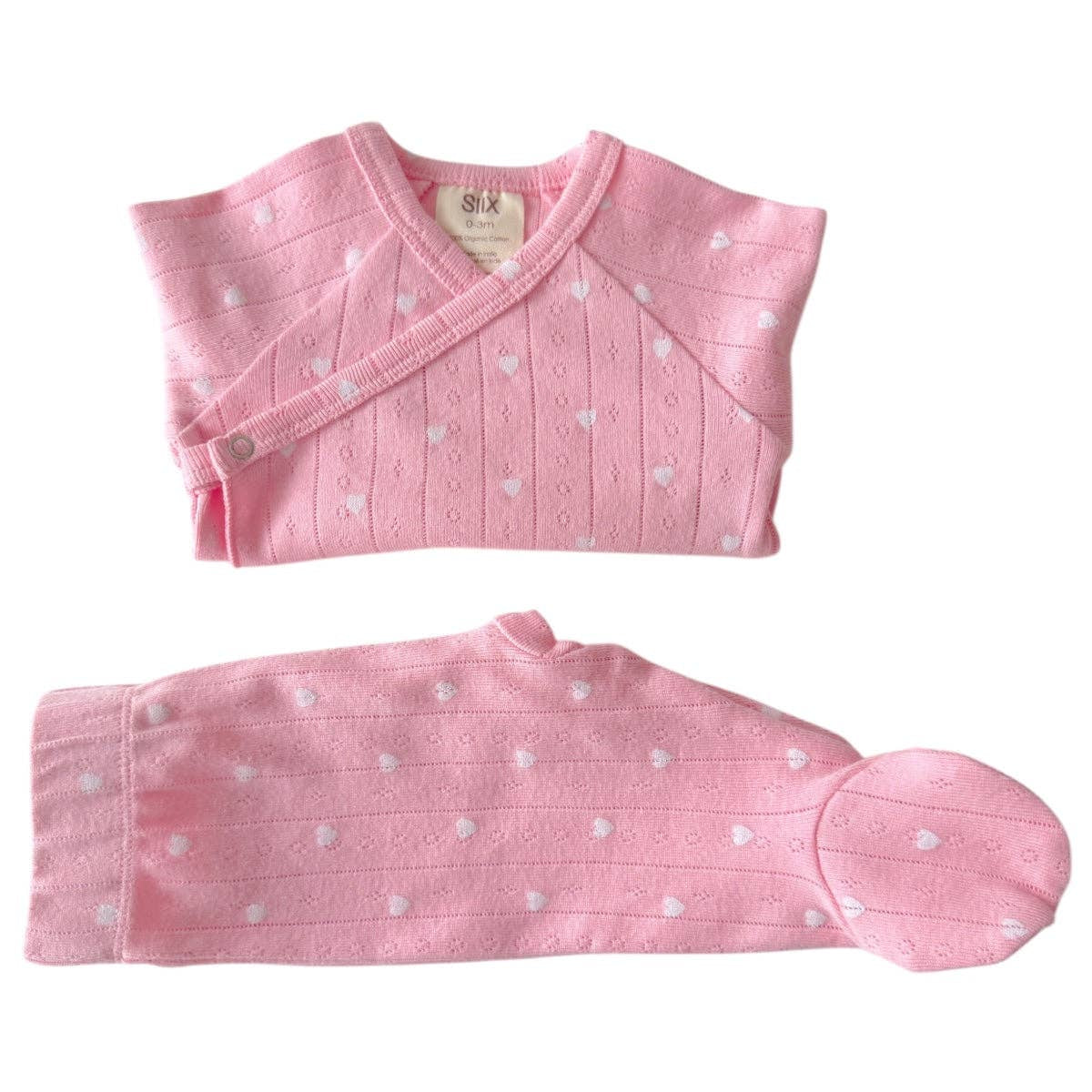 Pink baby outfit with white polka dots on a white background