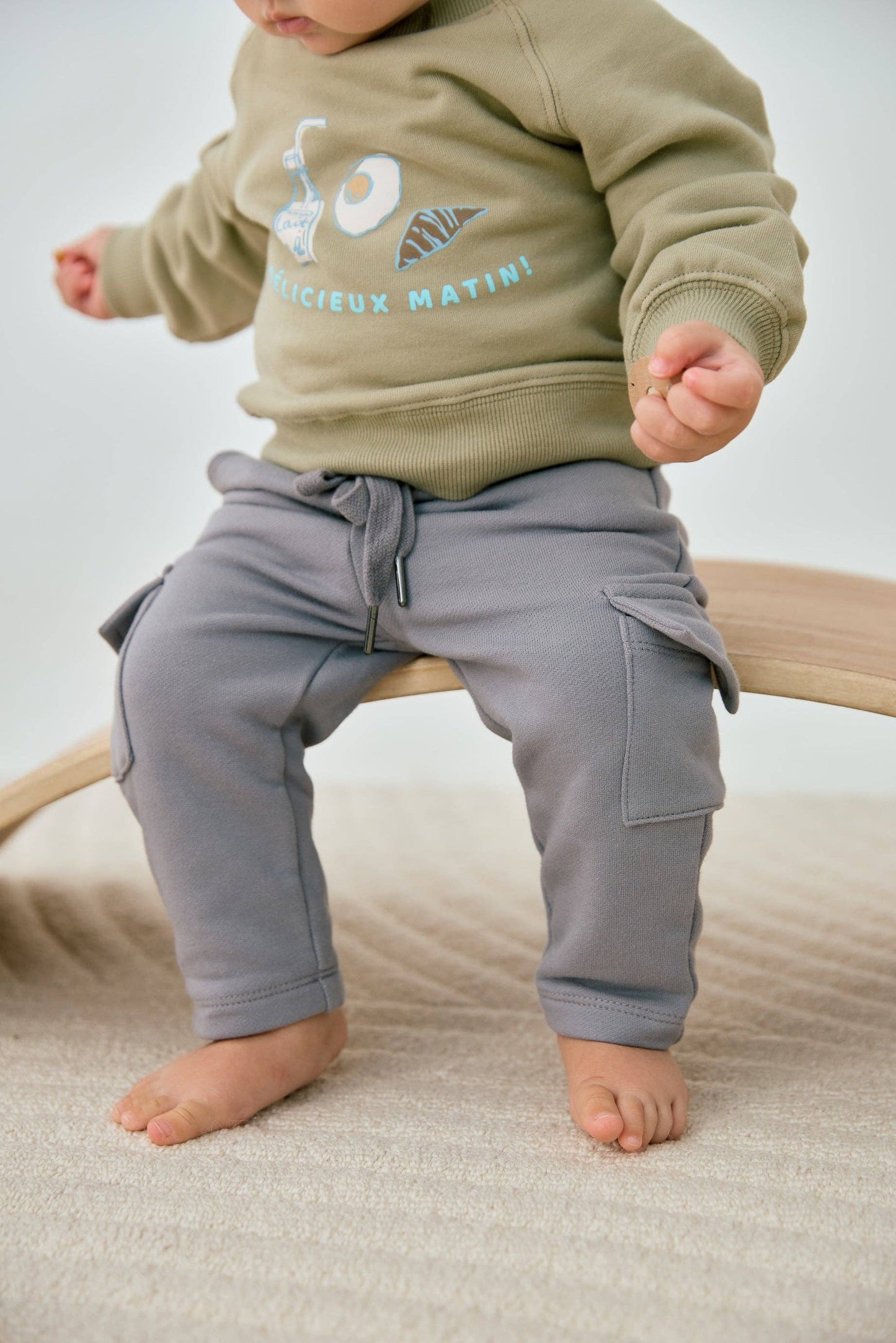 Child wearing a green sweatshirt with text and gray pants on a neutral background