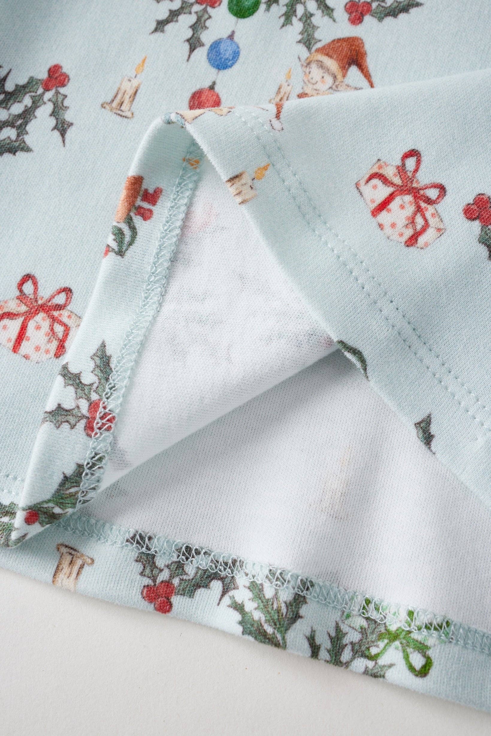 Christmas-themed fabric with reindeer, holly, and presents on a light blue background.