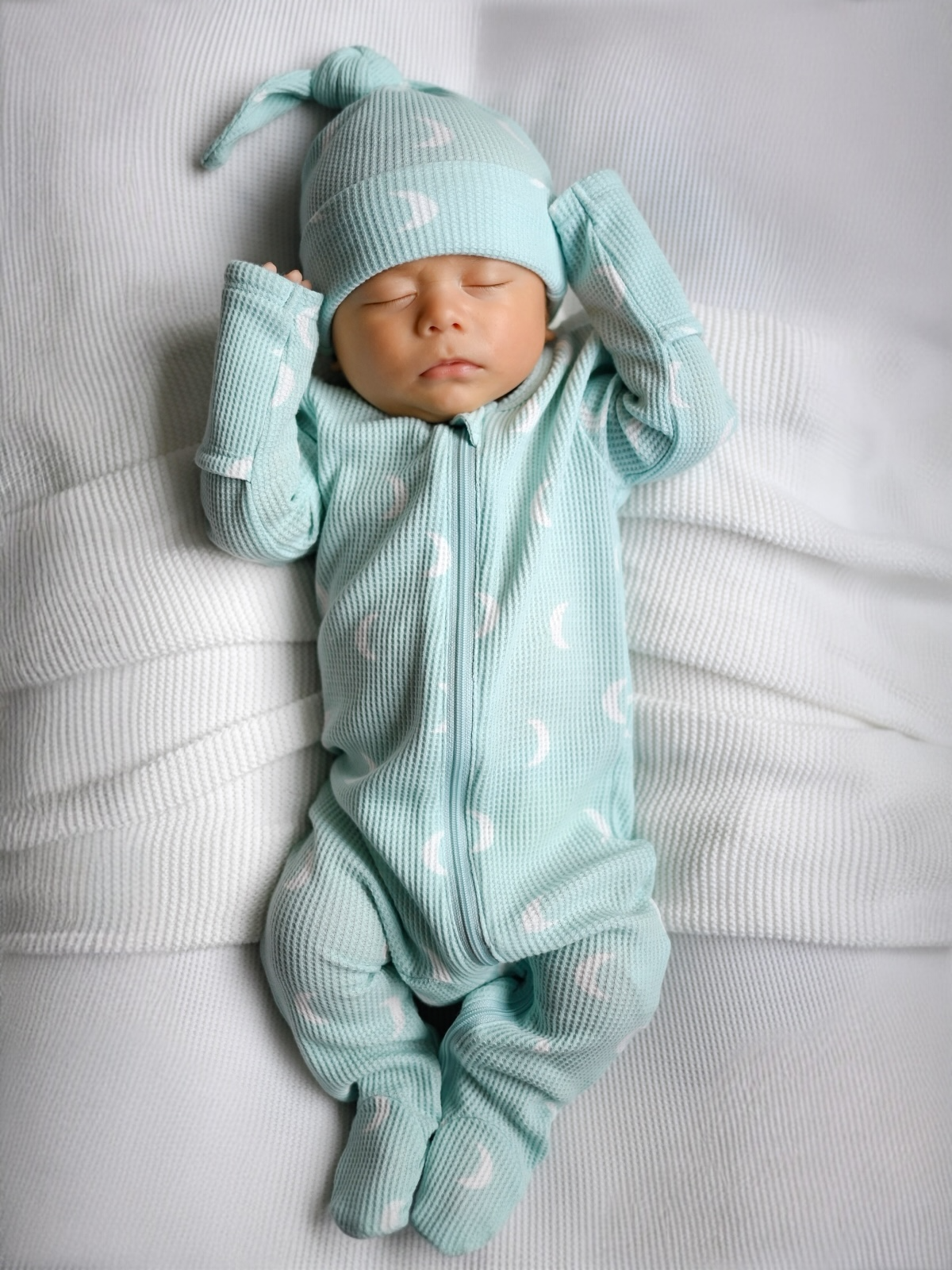 Newborn baby in a light green outfit with matching hat on a white background